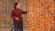 女子坐在门前，旁边挂着黄橙橙的柿子，画面真唯美